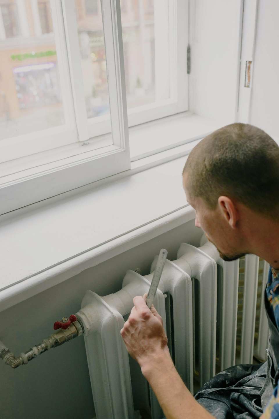 Vue de dessus d'un ouvrier masculin anonyme avec une règle près du radiateur et du rebord de la fenêtre dans la maison